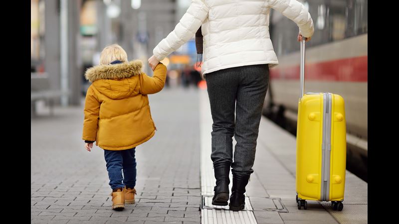 Woman holding her son's hand and a suitcase on a train station platform