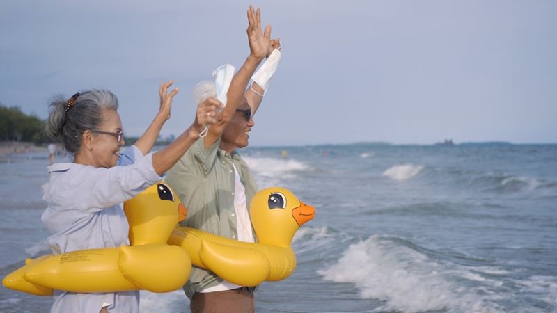 A couple by the sea with their arms raised and an inflatable duck rubber ring around their waists