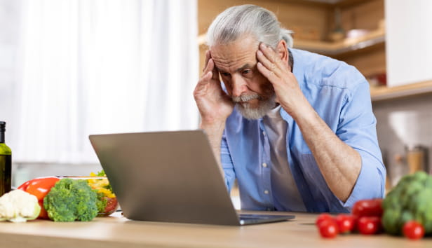 A man with his head in his hands staring at a laptop screen