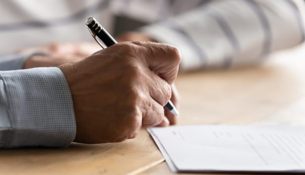 A person's hand holding a pen and writing on a piece of paper