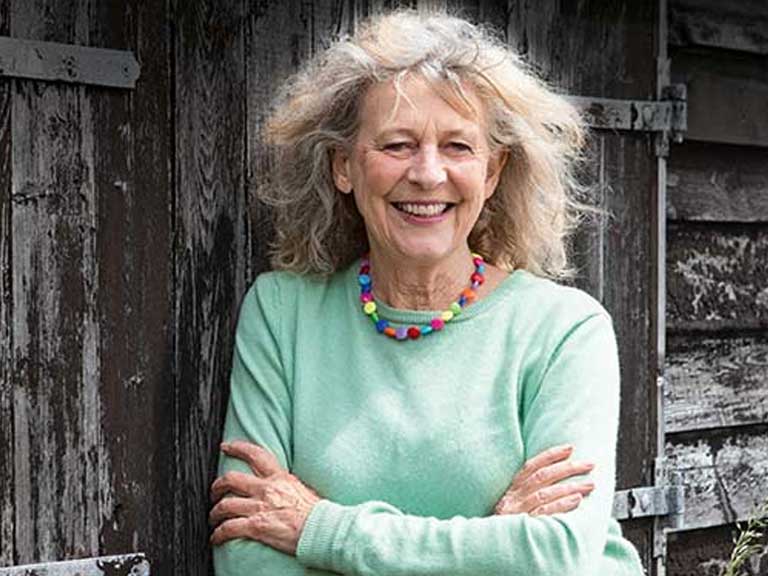 Deborah Moggach smiling and leaning against a wooden wall