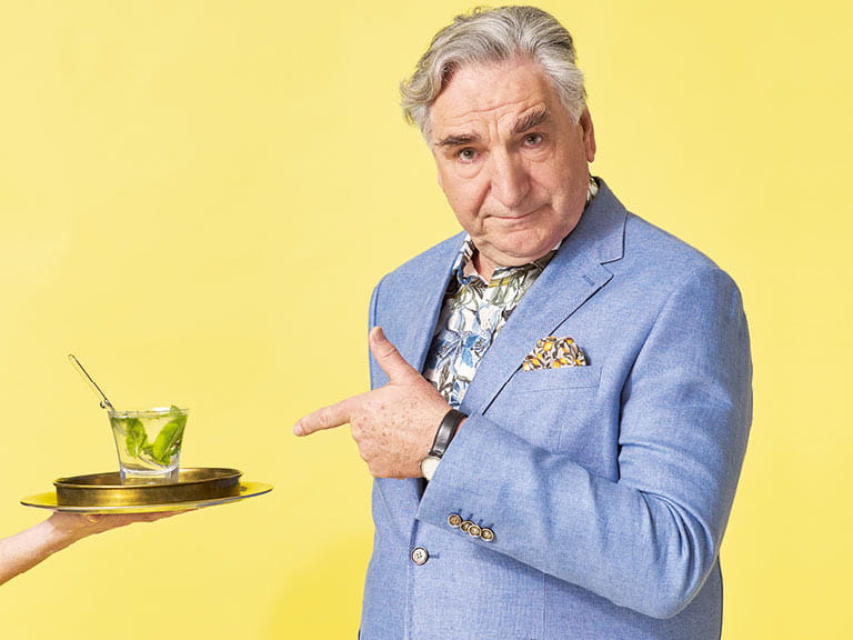 Jim Carter pointing at a serving tray with a cocktail on it.