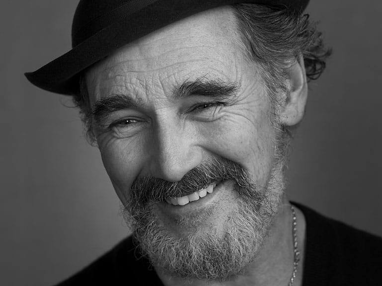 Black and white image of Mark Rylance smiling with a bowler hat on. Photographed by Pål Hansen.
