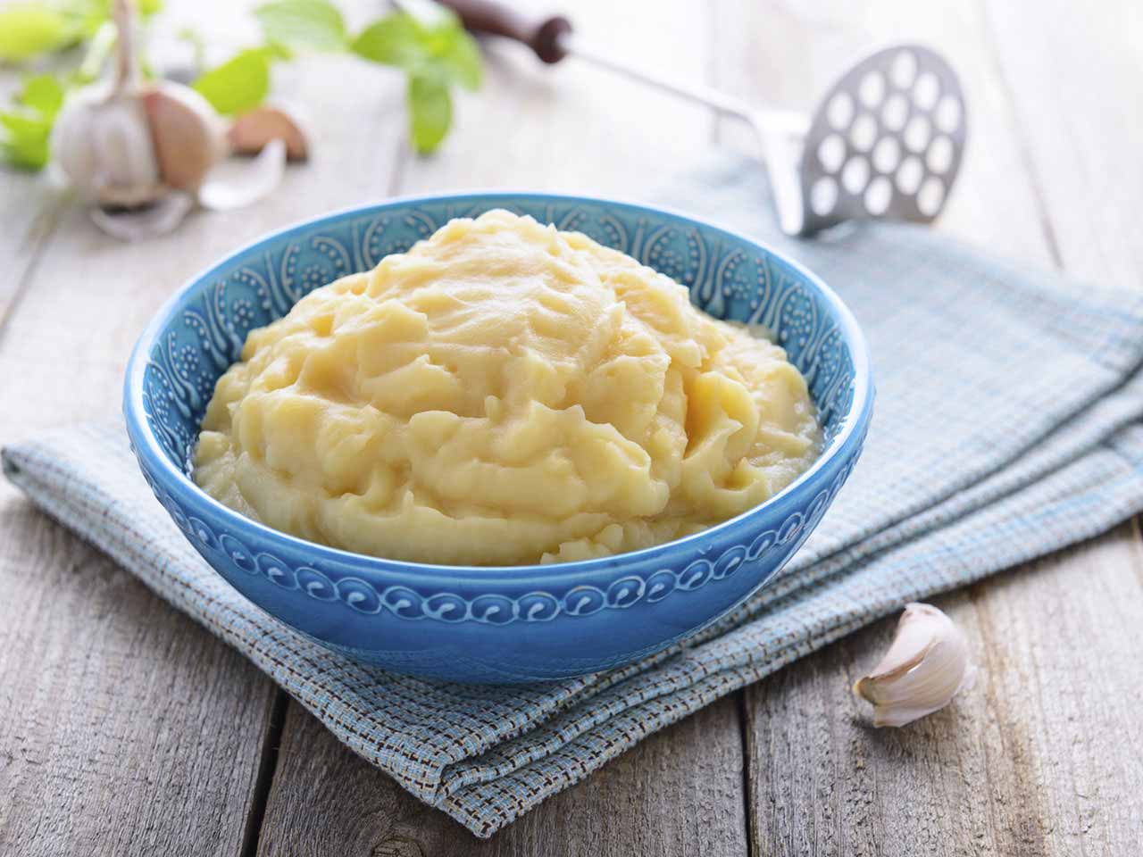 Bowl of mashed potato and a garlic clove on a wooden table