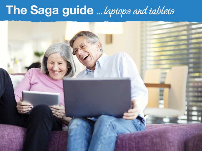 A woman and a man laugh as they look at a laptop and a tablet computer
