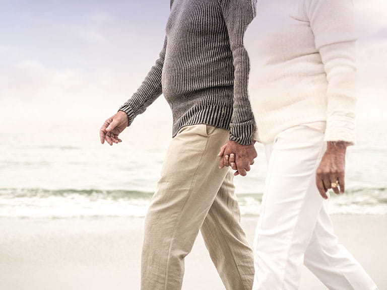 An older couple walk on the beach to highlight the importance of walking correctly