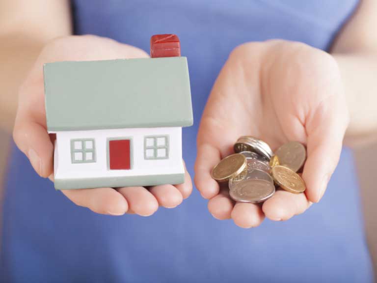 Woman holding a toy house in one palm, coins in the other palm