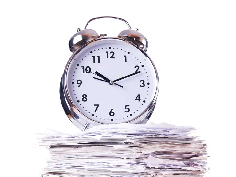 Alarm clock on a pile of paper to represent the submission deadline approaching