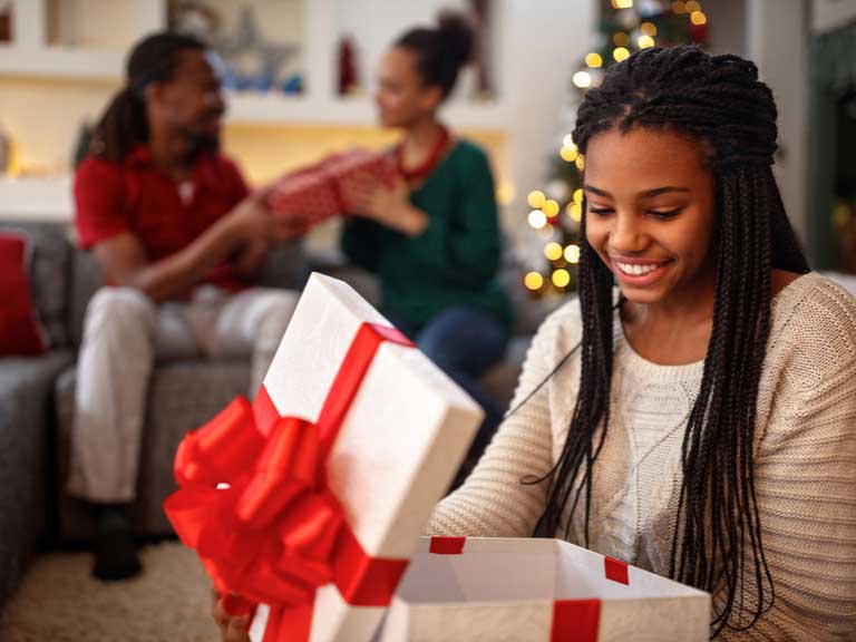 Teenager opening gift while her parents exchange gifts in the background