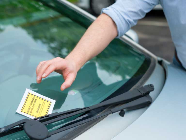 Man reaching over a car windscreen to pick up a parking fine notice stuck under the windscreen wiper