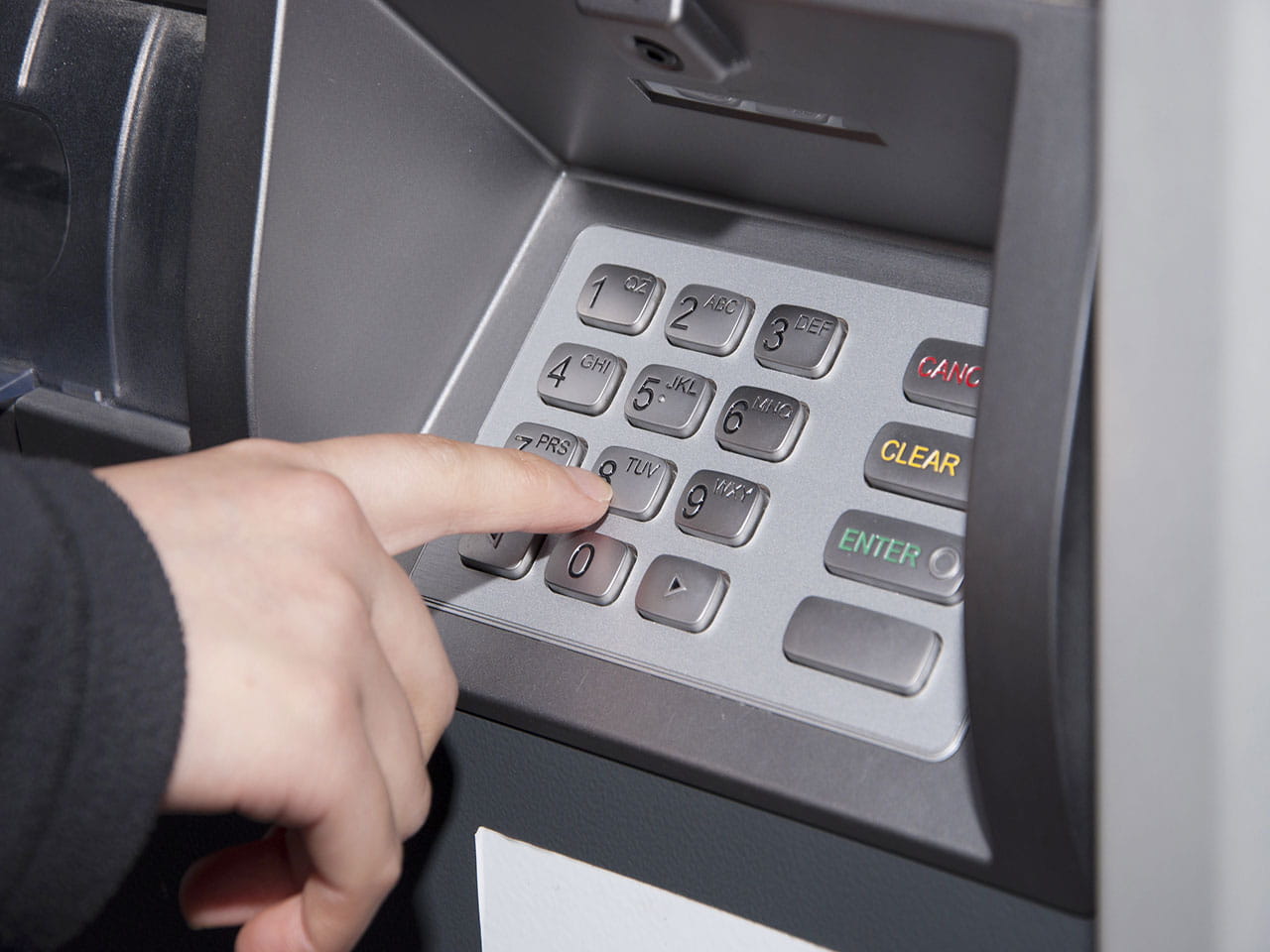 Person typing in their PIN at a cash machine 