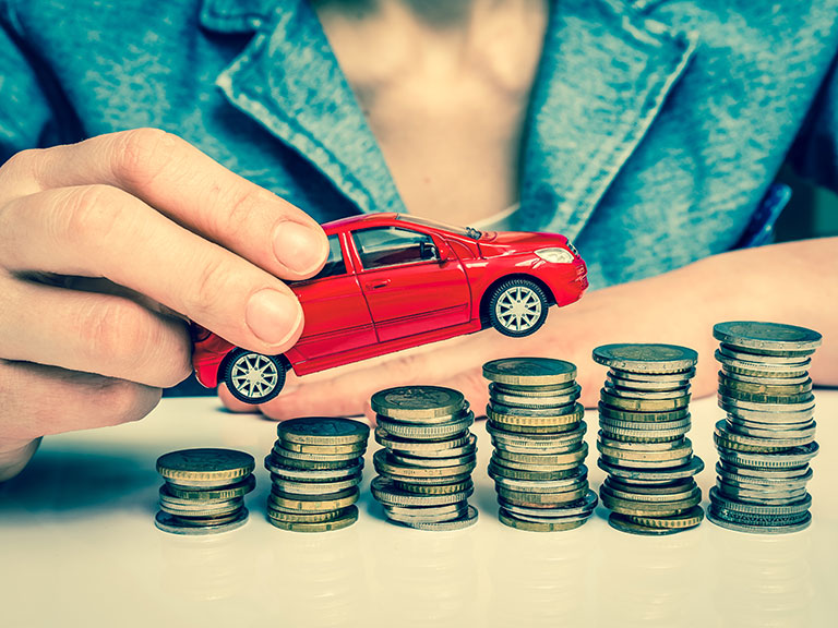 A car on piles of coins to represent being caught by a car leasing scam