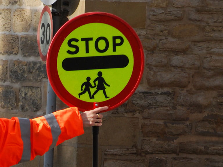 An arm of a lollipop person holding out the stop sign at a school crossing