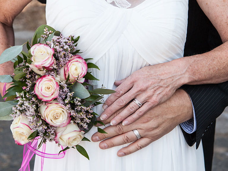 An older couple hold hands wearing wedding rings