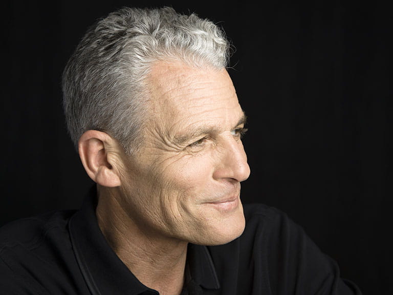 A handsome older man with grey hair smiles off camera