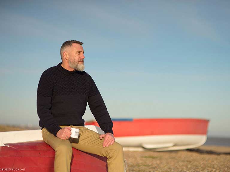 An older man wears his Shackleton replica sweater on a cold beach