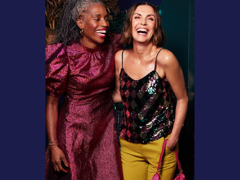 The model on the left is wearing a puff sleeved, dark pink dress and the model on the right is in a sequined multicoloured strappy top with mustard yellow trousers.