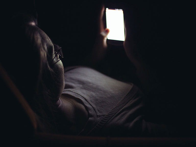 An older woman reads her phone in bed because she can't sleep