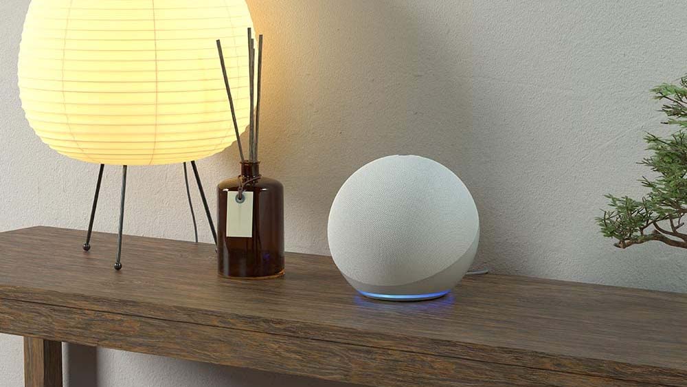 An Amazon Echo Dot device displayed on a side table with a lamp and diffuser
