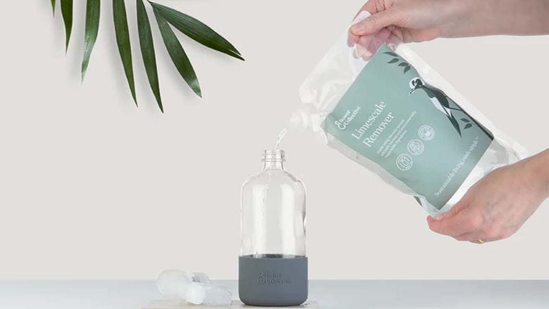 A packet of limescale remover being poured into a reusable glass bottle