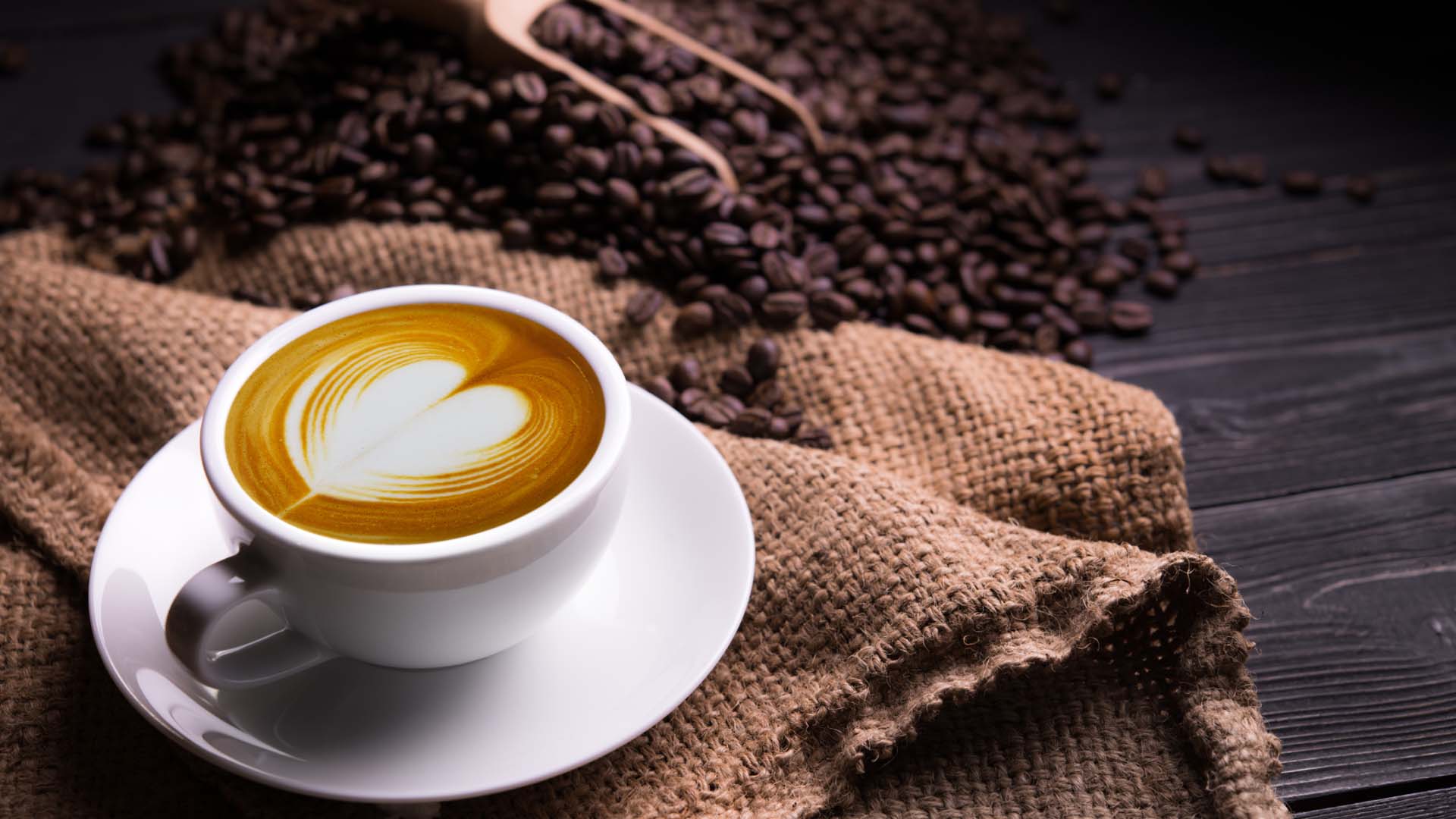 Close-up of a cup of coffee styled with a hessian bag and a pile of coffee beans in the background.