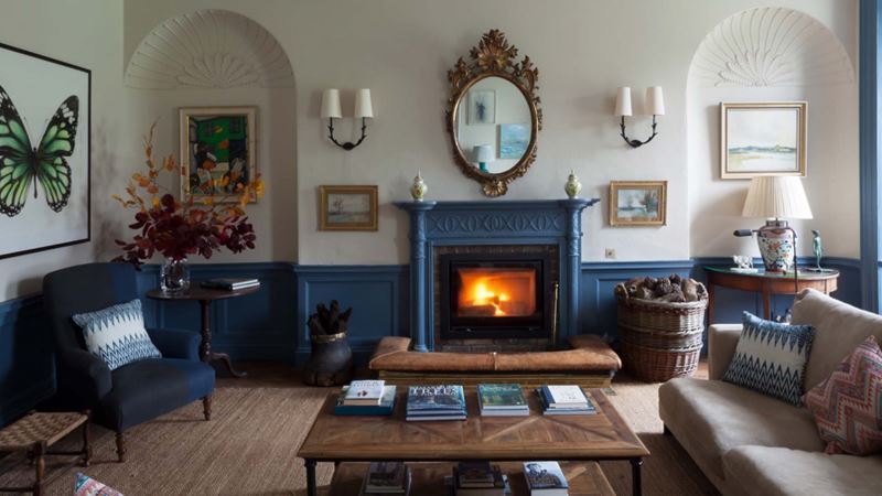 A sitting room in an old house with a contrasting deep blue and off-white colour scheme, with traditional furniture and a roaring fireplace