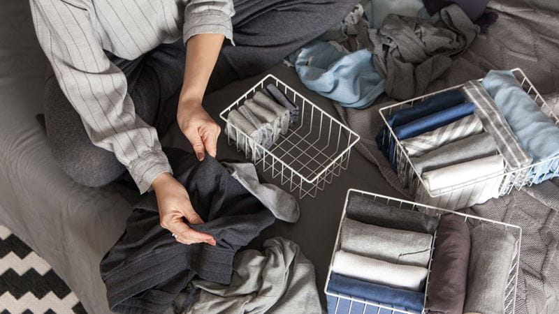 Someone sitting cross-legged on a bed organising clothes into storage baskets