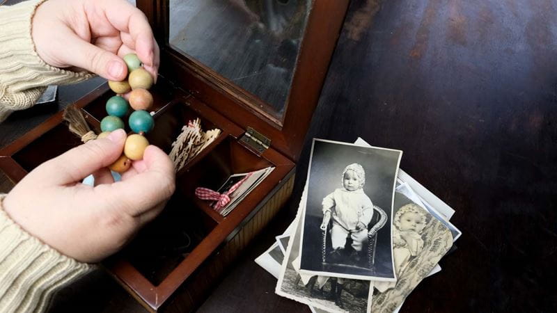 Close-up of a trinket box with hands holding a bracelet and old photographs next to a wooden box