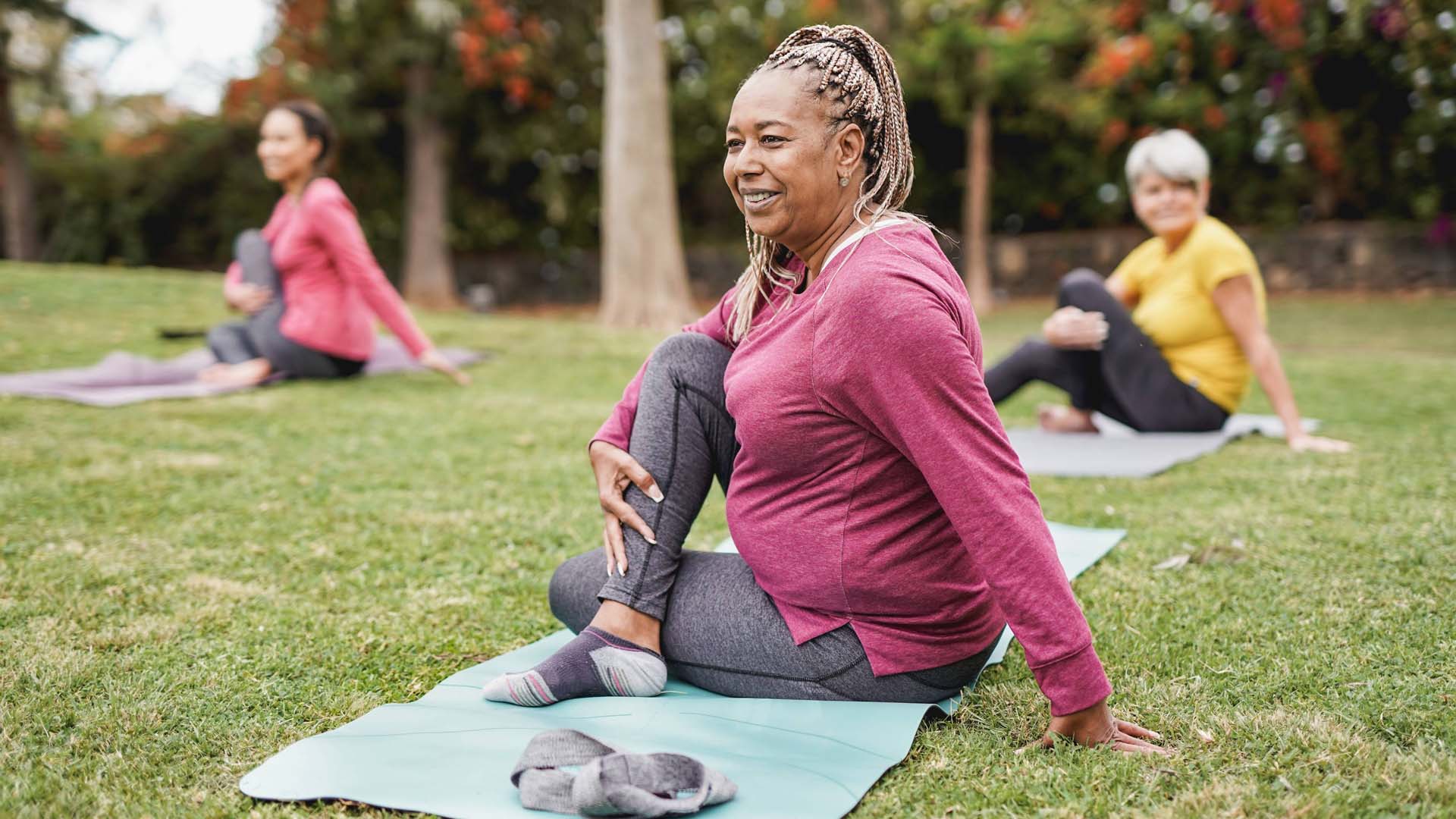 A group of women in sports attire practising yoga in a part setting with lots of space between them
