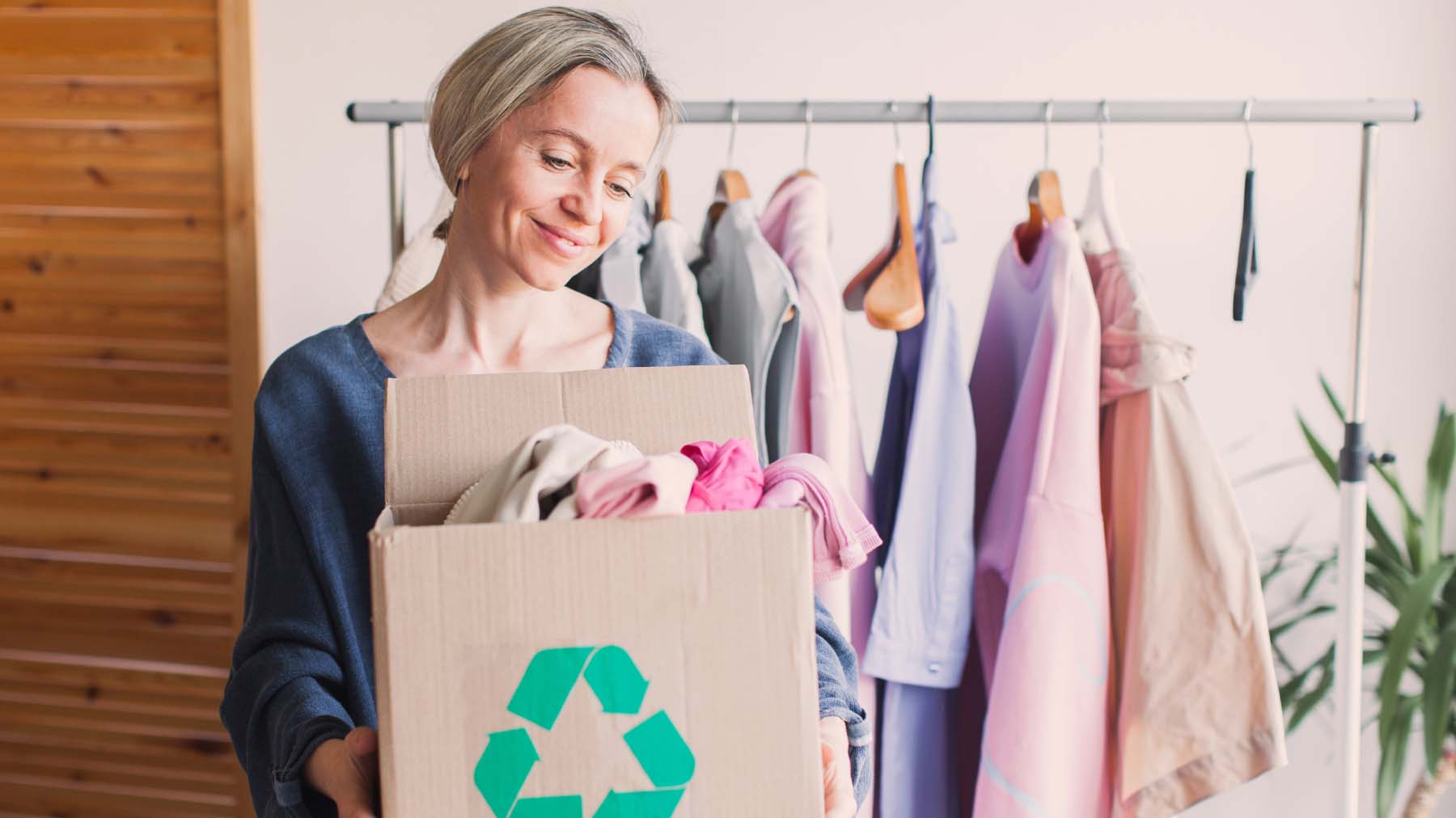A woman holding a cardboard box bearing a recycling symbol which is full of clothes.