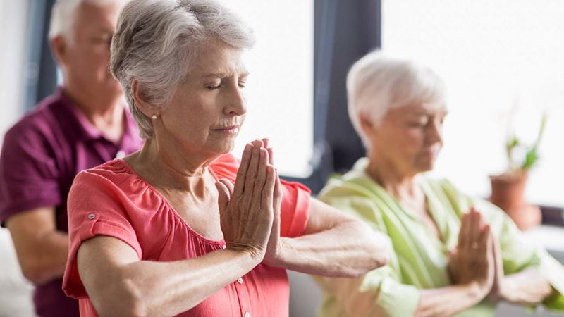 Mature people practising a relaxing yoga pose with their eyes closed and palms pressed together in front of their chests