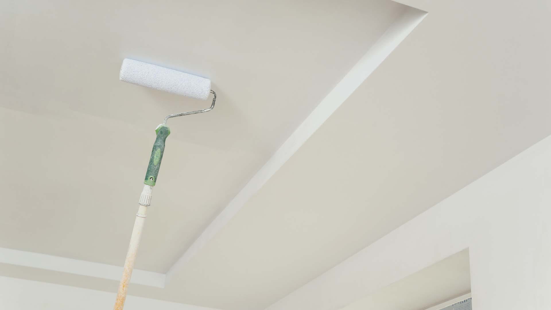 A roller on a pole painting a ceiling white