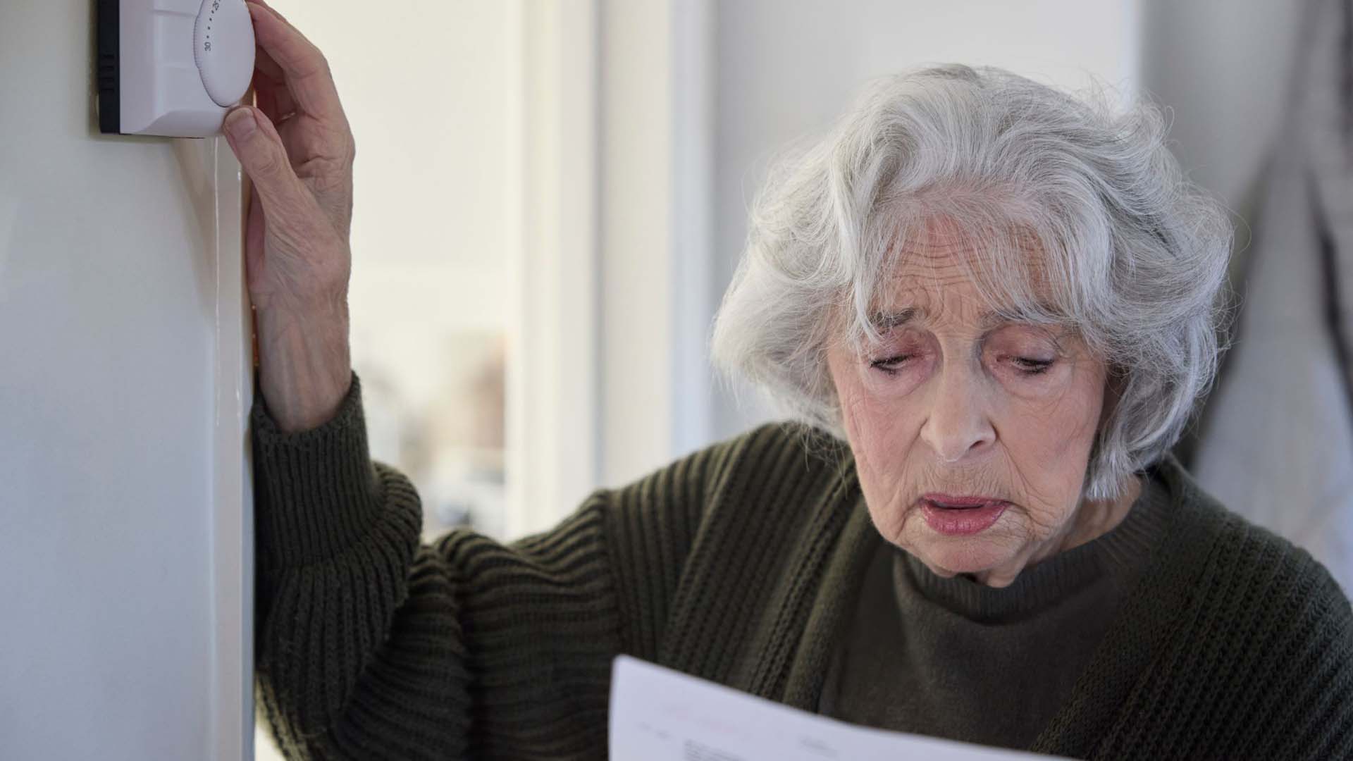 Older lady turning down her thermostat