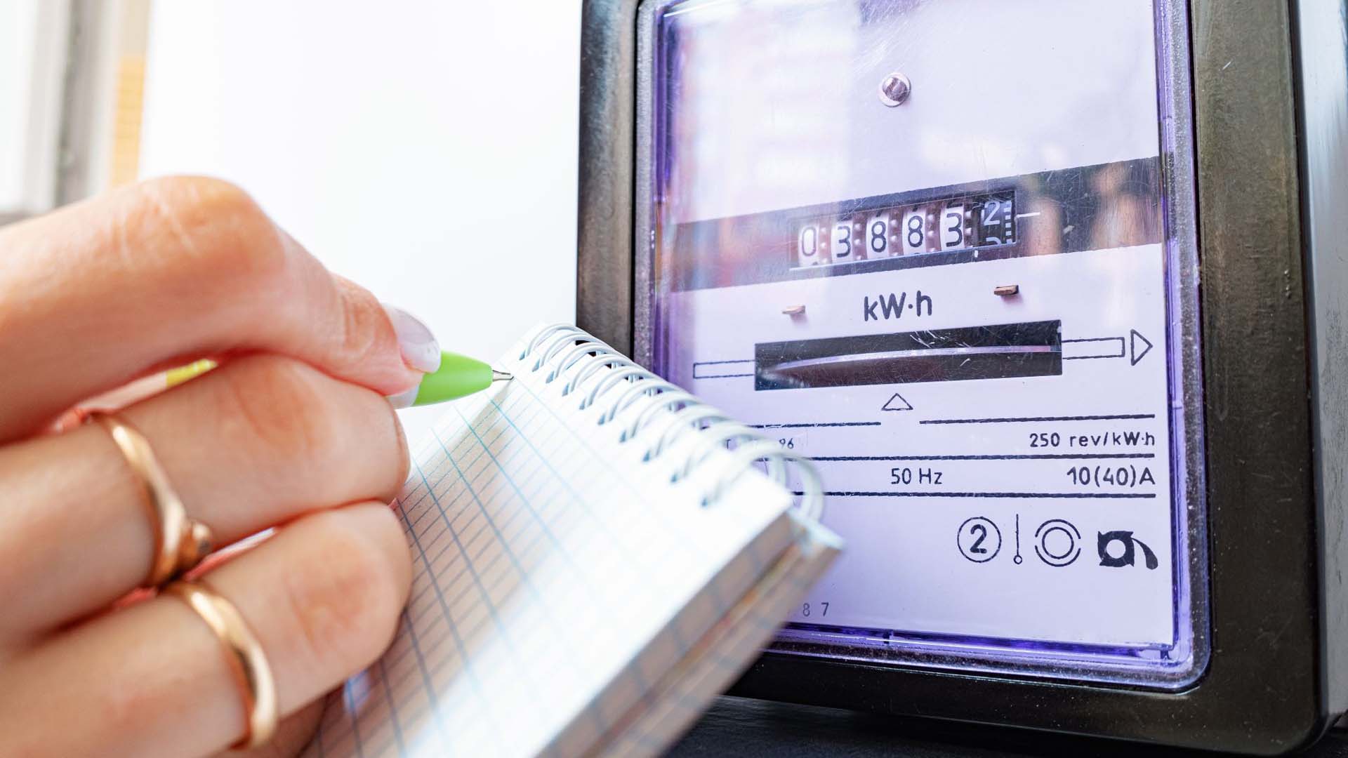 a close up of a meter with a woman writing down the reading on a pad of paper