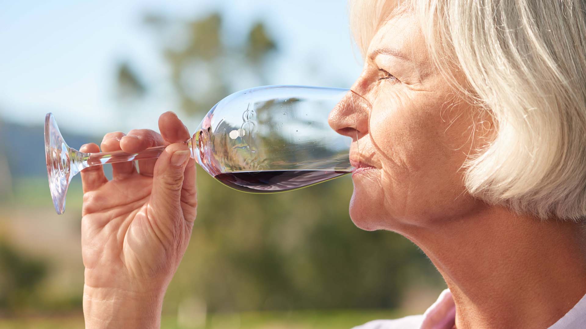 An older woman drinking a glass of red wine