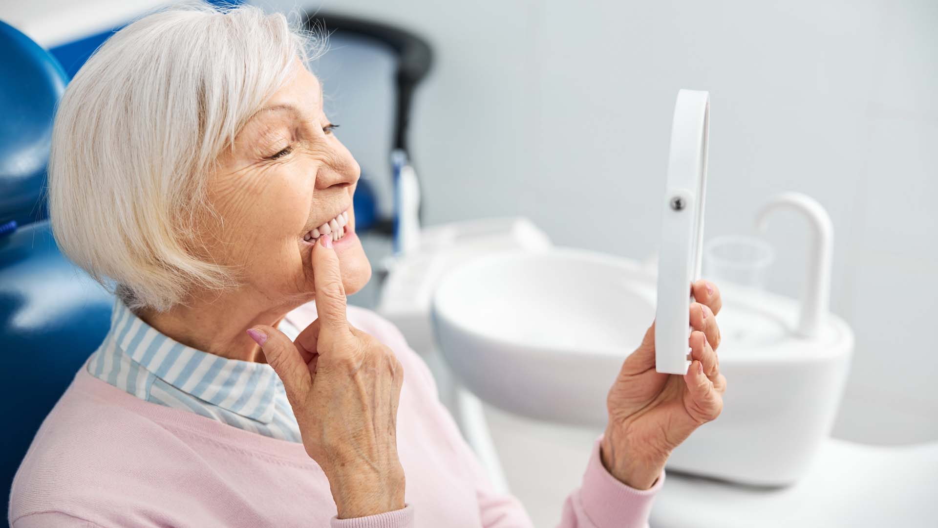 An older woman inspects her teeth in a mirror