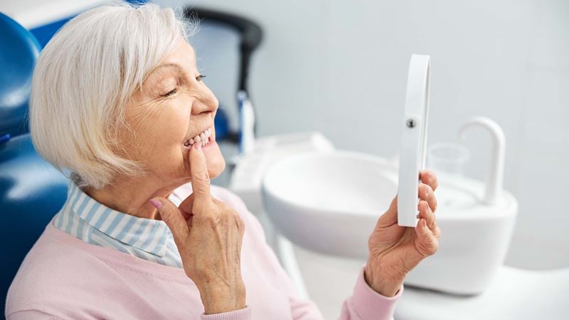 An older woman inspects her teeth in a mirror