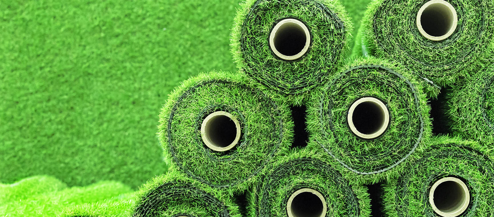 Rolls of artificial grass stacked on each other with more artificial grass in the background
