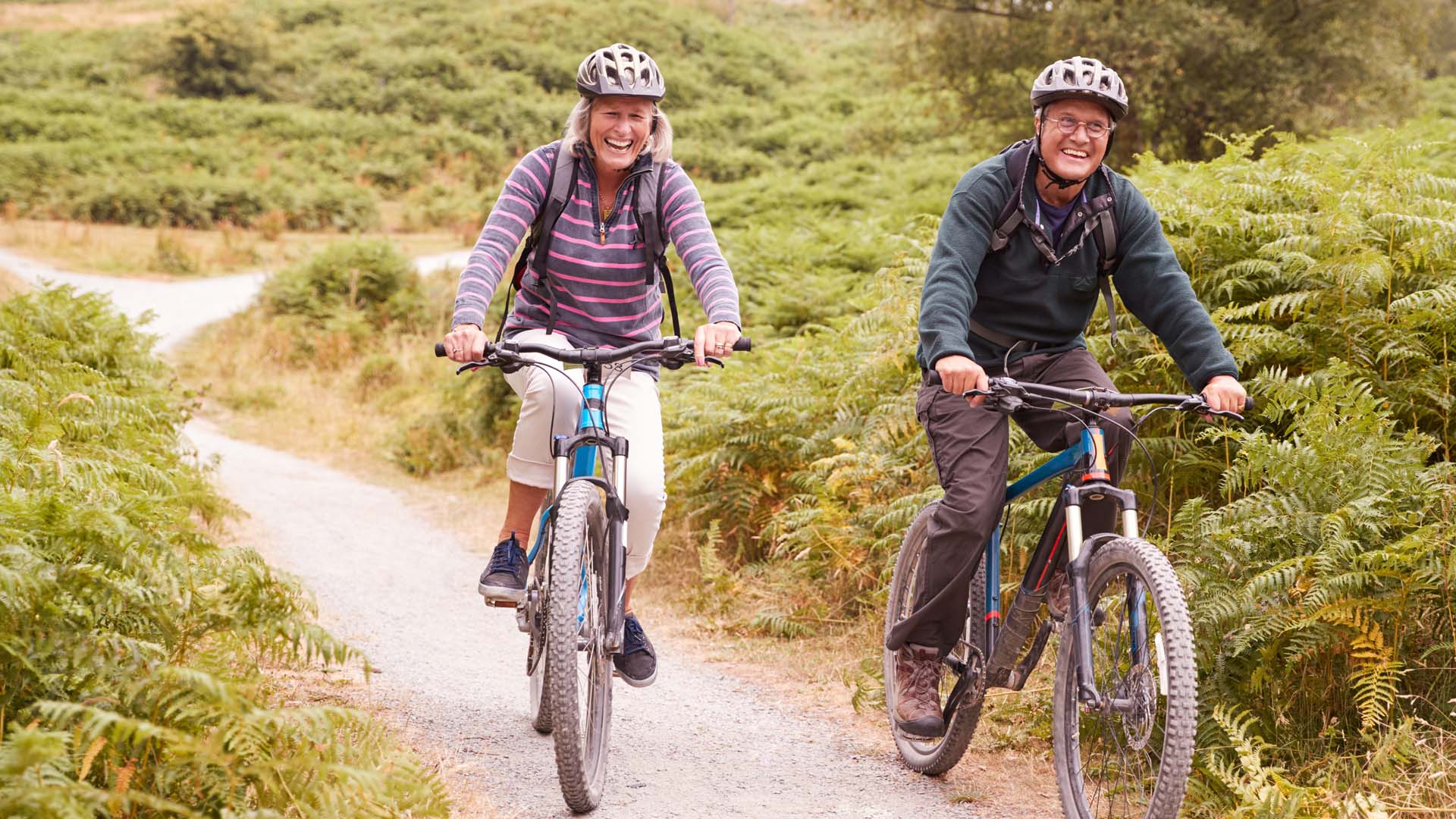 Two mature adults cycling along a path wearing winter jackets and helmets