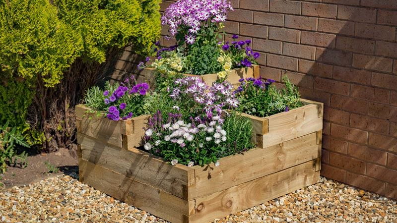 A square wooden raised bed with beautiful, colorful spring flowers arranged in three levels