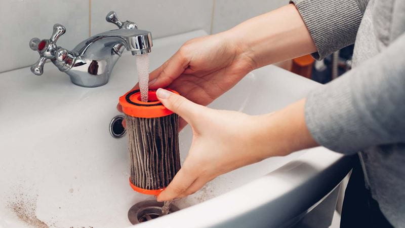 someone running a vacuum cleaner filter under a tap in a sink
