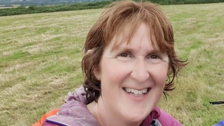 Close-up of a woman smiling; Kath Needham wears a waterproof jacket in the outdoors