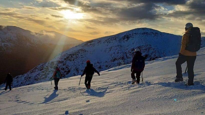 Hikers descend a snowy mountain as the sun begins to set