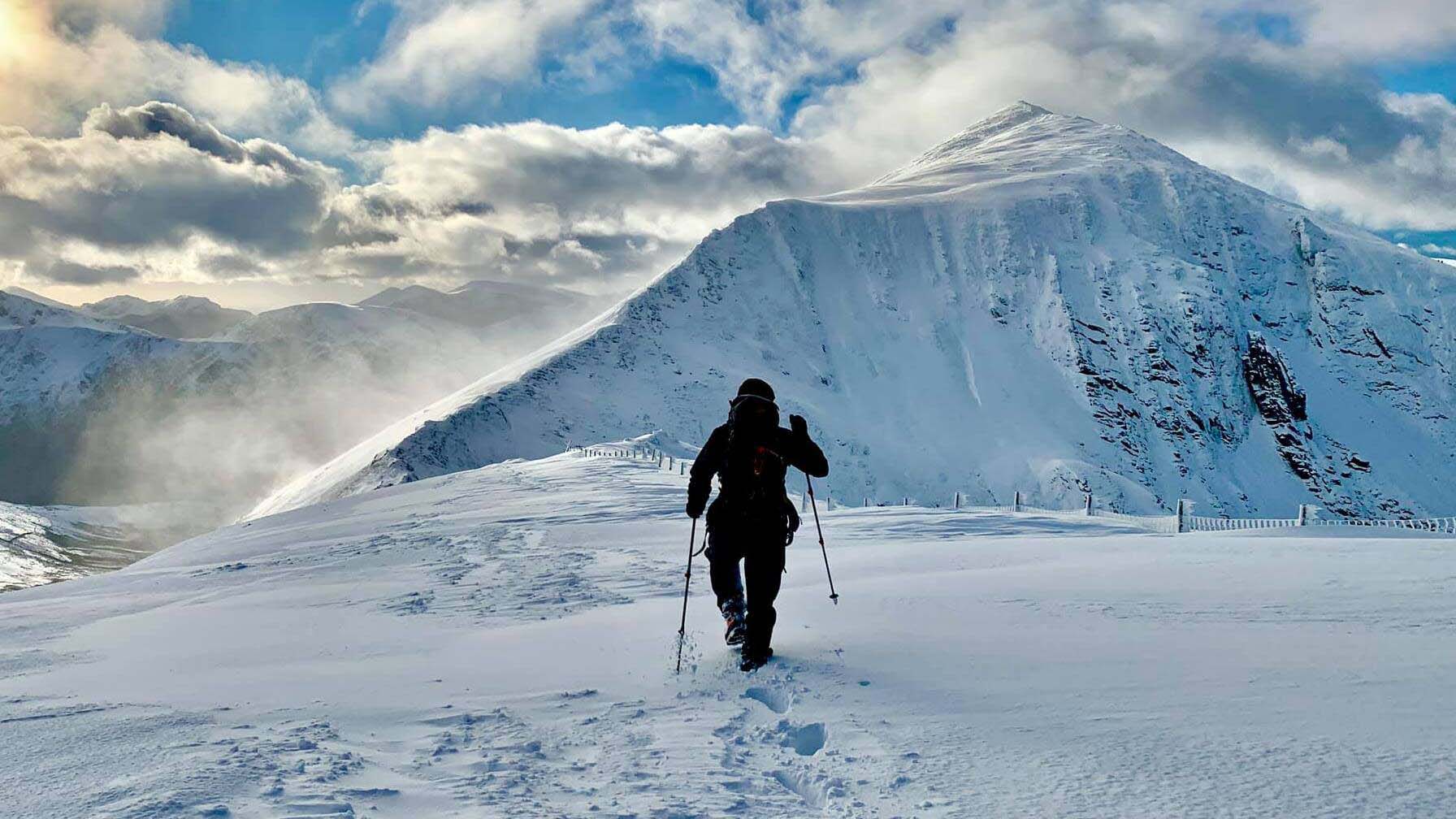 A hiker walks away, heading for the snowy mountain ahead