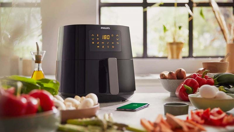 A black air fryer on a kitchen counter surrounded by healthy food