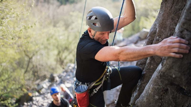 A man in a helmet rock climbing with ropes an a harness outdoors
