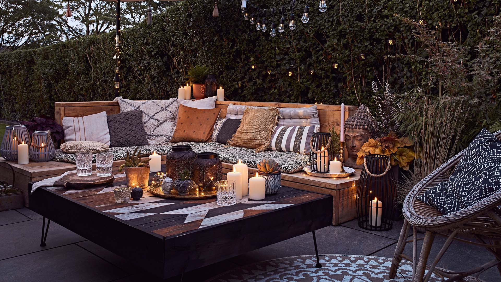 Garden bench covered with cushions and coffee tables laden with candles 