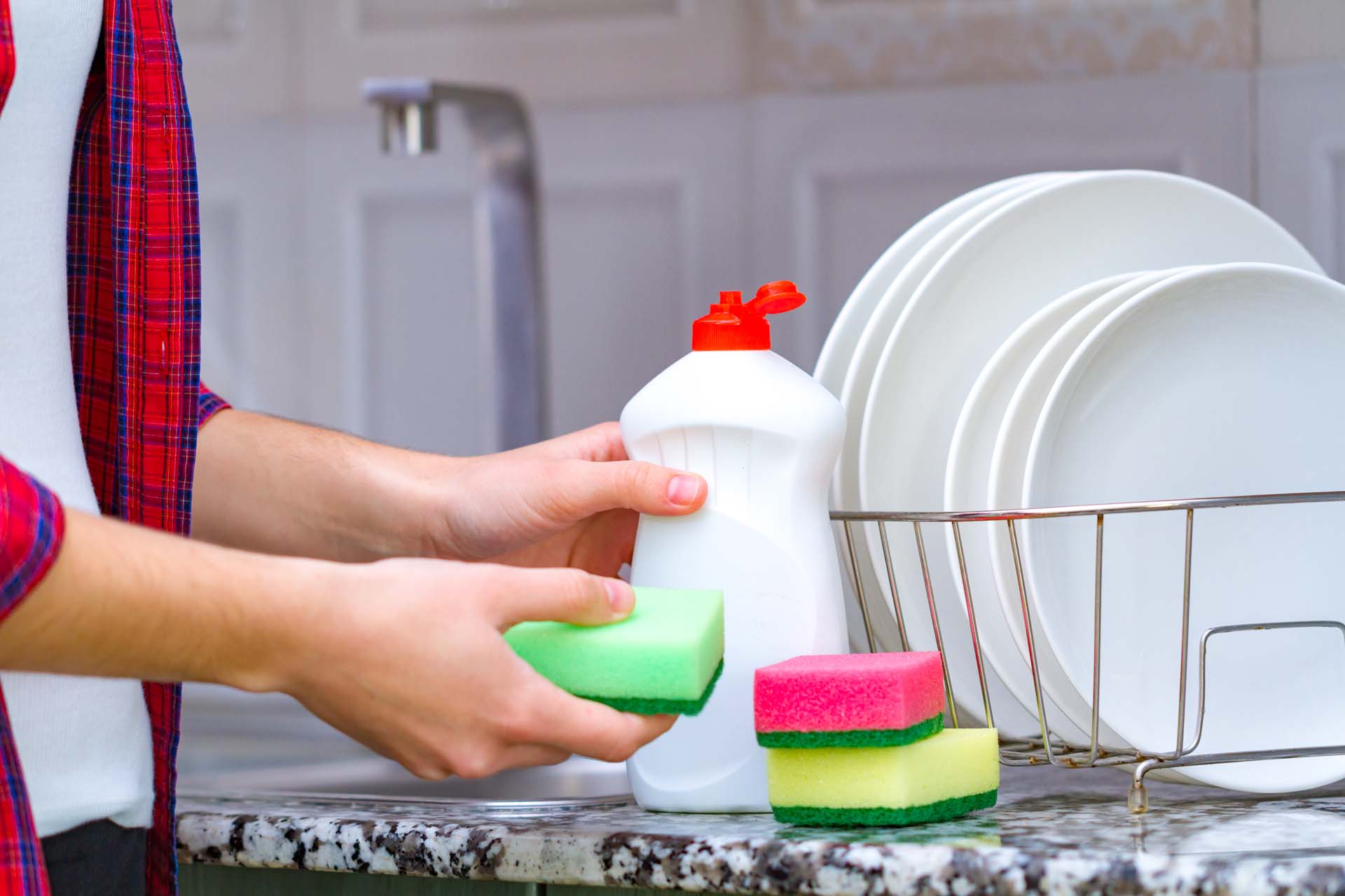 A hand doing the washing up manually using a sponge and washing up liquid