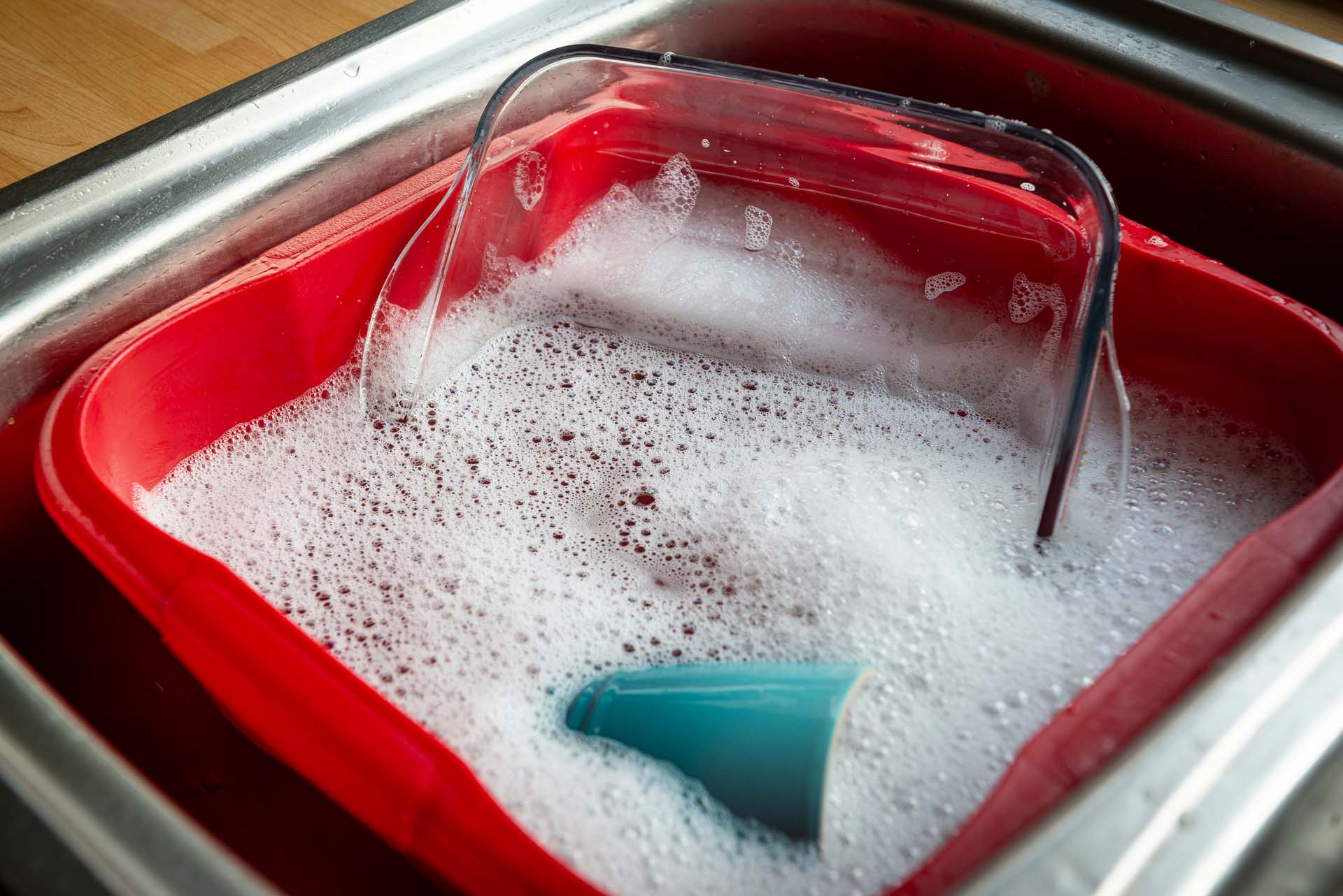 A glass dish being washed in a washing up bowl full of soapy bubbles