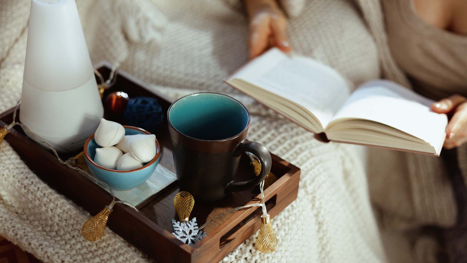 someone reading a book in bed with a tray laid out in front of them with tea